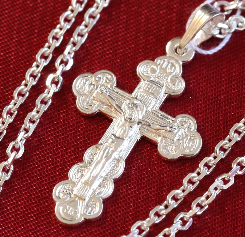 May include: A silver chain necklace with a detailed silver cross pendant. The cross features a figure of Jesus Christ and intricate floral designs.
