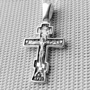 Könnte beinhalten: Ein silberfarbener Anhänger in Form eines Kreuzes. Das Kreuz zeigt eine detaillierte Darstellung von Jesus Christus und religiösen Inschriften. Der Anhänger hat eine Schlaufe für eine Kette und ist vor einem strukturierten Hintergrund platziert.