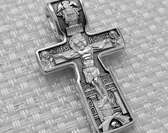 May include: A silver cross pendant with intricate details. The cross features a depiction of Jesus Christ on the crucifix, surrounded by various religious figures and symbols.