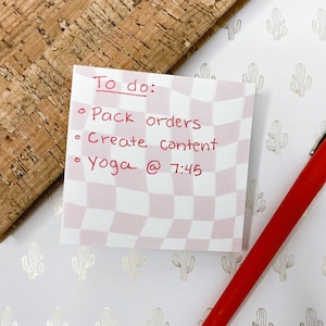 May include: A pink and white checkered sticky note with a to-do list written in red ink. The list includes "Pack orders", "Create content", and "Yoga @ 7:45".