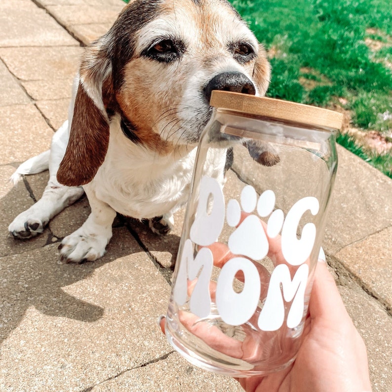Pode incluir: Um frasco de vidro transparente com tampa de madeira e um adesivo de vinil branco que diz "Dog Mom" com uma pegada de pata.