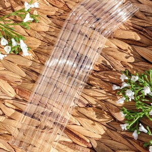 Pode incluir: Um conjunto de canudos de vidro transparente com uma curva na parte superior. Os canudos est&atilde;o dispostos em forma de leque sobre uma superf&iacute;cie de vime marrom.
