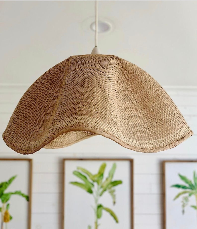 May include: A woven, light brown, lampshade with a scalloped edge hangs from a white cord. The lampshade is made of natural materials and has a rustic, organic look.