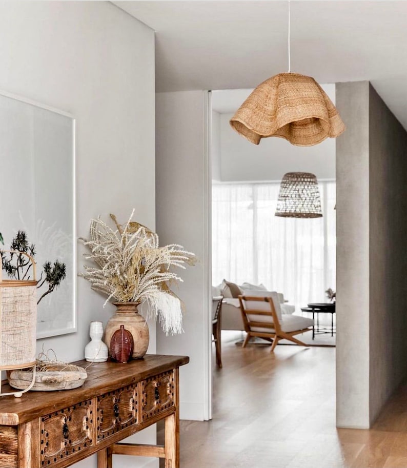 May include: A wooden console table with three drawers, a vase with dried flowers, and a woven lampshade hanging from the ceiling. The table is in a hallway with a white wall and a doorway leading to another room.