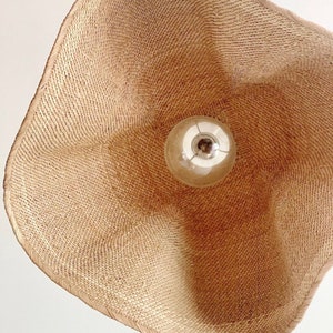 May include: A woven wicker lampshade with a light bulb inside. The lampshade is a light brown color and has a natural, organic texture.