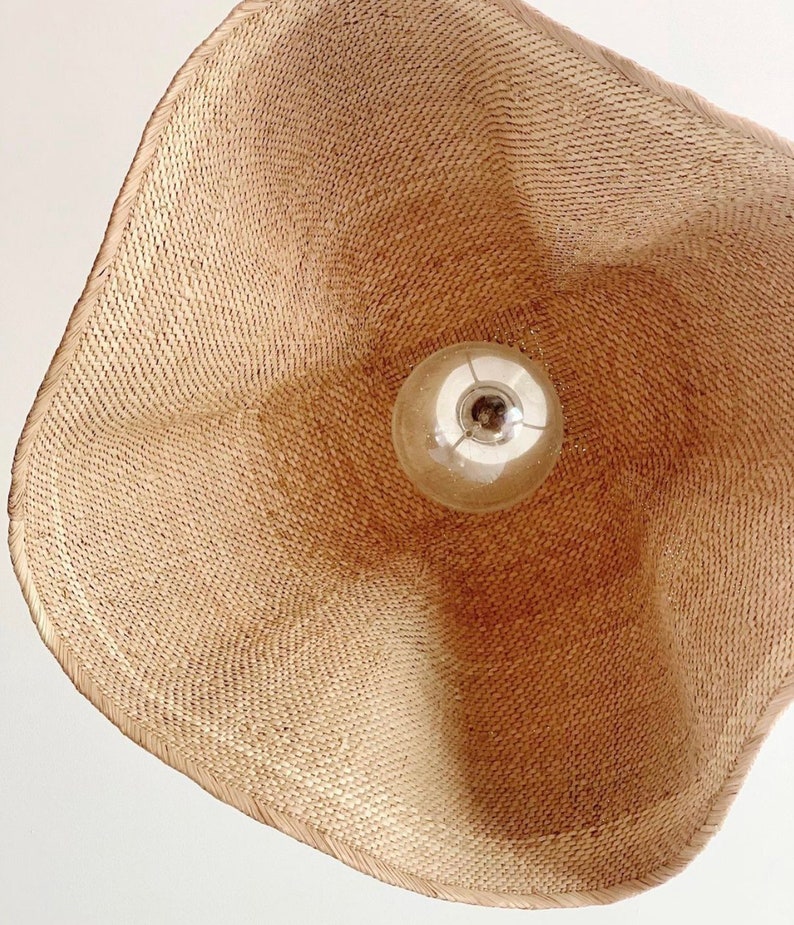 May include: A woven wicker lampshade with a light bulb inside. The lampshade is a light brown color and has a natural, organic texture.