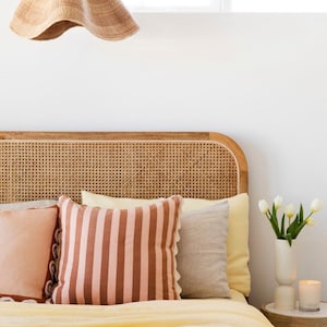 May include: A bedroom with a bed featuring a woven headboard, a yellow and pink striped pillow, and a white vase with white tulips on a wooden nightstand.