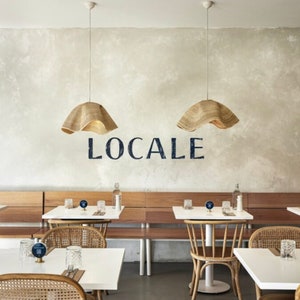 May include: A restaurant interior with white tables and chairs, wooden benches, and woven pendant lights. The restaurant is called "LOCALE" and is decorated in a minimalist style.
