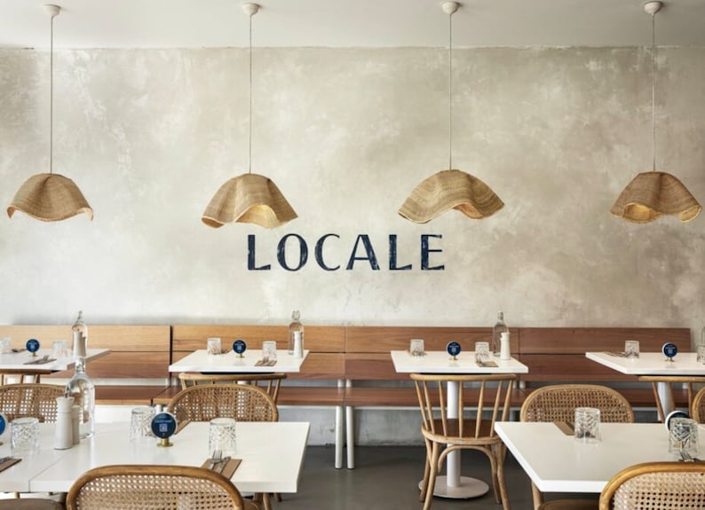 May include: A restaurant interior with white tables and chairs, wooden benches, and woven pendant lights. The restaurant is called "LOCALE" and is decorated in a minimalist style.