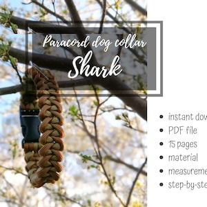 May include: A brown and tan paracord dog collar with a black buckle, suspended from a tree branch. The text "Paracord dog collar Shark" is displayed above the collar. The background shows a blurred tree with white blossoms.