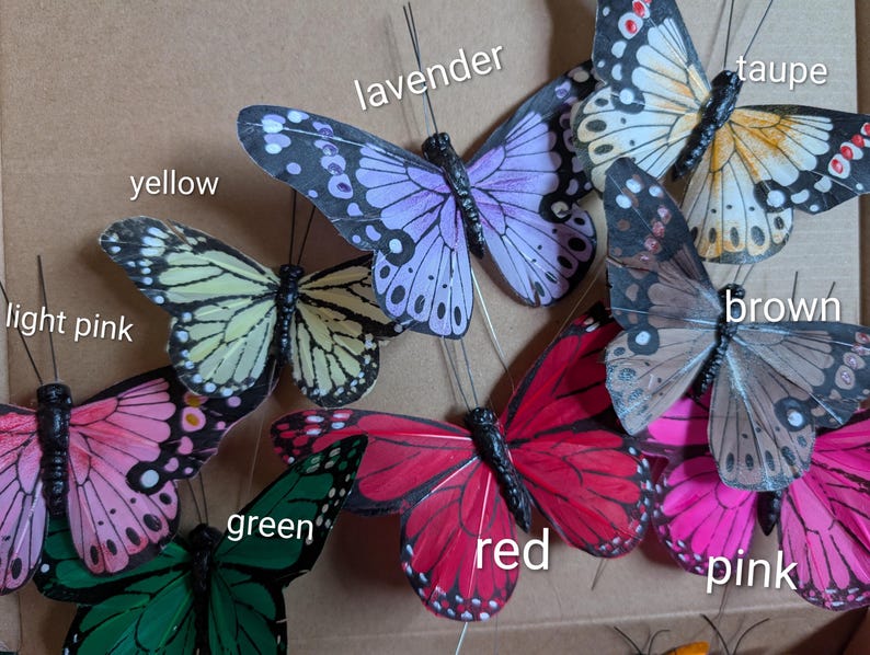 Peut inclure: Une collection de papillons d&eacute;coratifs artificiels dans diverses couleurs, notamment rose clair, jaune, lavande, taupe, marron, vert, rouge et rose. Chaque papillon pr&eacute;sente de fines antennes en fil de fer et des motifs d'ailes d&eacute;taill&eacute;s.