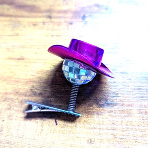 Peut inclure: Une pince à cheveux fantaisie avec une mini boule disco, un chapeau de cowboy violet et une pince argentée. La boule disco est montée sur un ressort. Le chapeau est d'un violet vif et brillant.