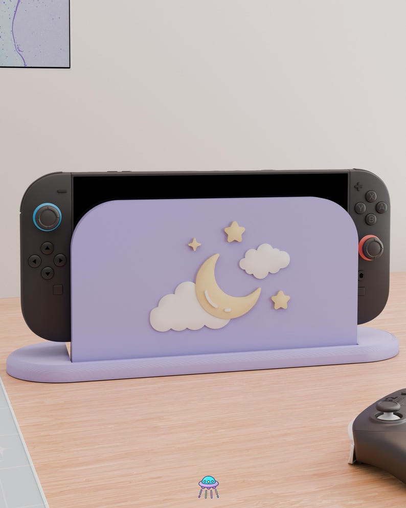 May include: A lavender gaming console dock featuring a raised, three-dimensional design of a pale yellow crescent moon, white clouds, and small yellow stars on the front panel. The dock holds a black gaming console with dark gray controllers.