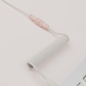 May include: A white coiled keyboard cable with a light pink connector. The cable is connected to a white keyboard. The image is set against a light pink background. The cable is a USB-C type.