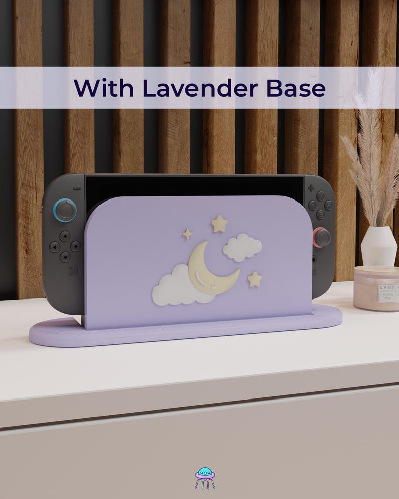 May include: A lavender-colored game console stand with a crescent moon, stars, and cloud design. The stand holds a black game console with blue and red accents. The text "With Lavender Base" is displayed above the stand.