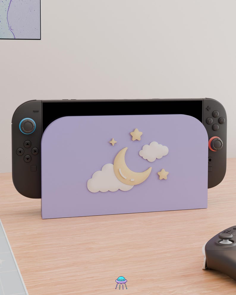 May include: A lavender gaming console dock featuring a raised, cream-colored crescent moon, two white clouds, and two small stars. The dock is attached to a black handheld gaming console with dark gray controllers, one with a blue ring and one with a red ring.