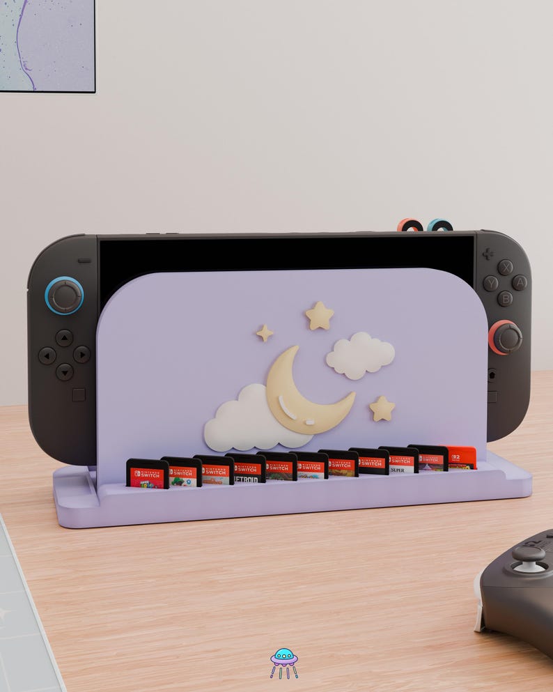 May include: A light purple gaming console dock featuring a crescent moon, two clouds, and two stars on the front panel. The dock includes a row of slots for ten game cartridges and holds a black gaming console with dark gray controllers attached.