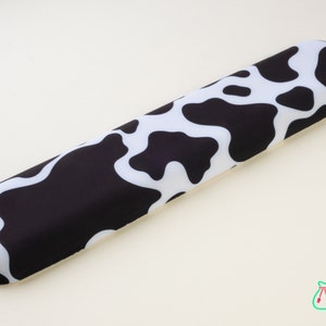 Könnte beinhalten: Eine schwarze und weiße Kuhfell-Handgelenkauflage für eine Tastatur. Die Handgelenkauflage besteht aus weichem, bequemem Material und ist so konzipiert, dass sie Ihre Handgelenke beim Tippen unterstützt.