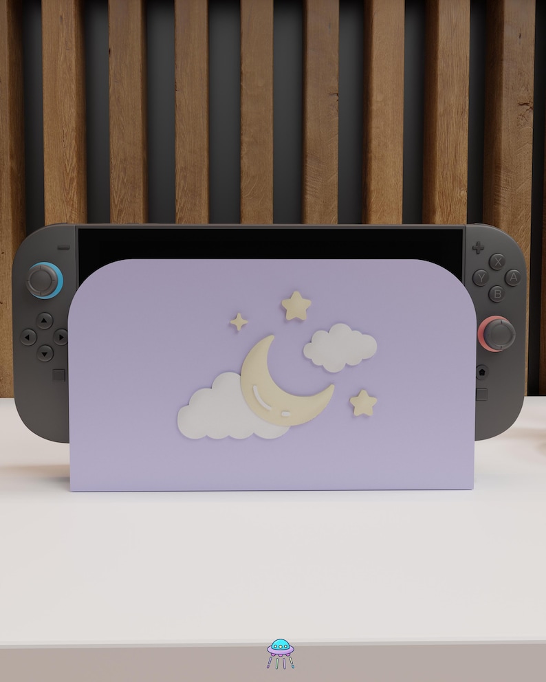 May include: A gray Nintendo Switch console with a lavender stand featuring a crescent moon, stars, and clouds. The stand is designed to hold the console upright. The background has a wooden slat design.