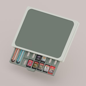 May include: A grey and white Nintendo Switch game storage case with a pull-out tray. The tray holds several game cartridges, and the case has slots for game accessories. The case is on a light pink background.