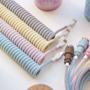 May include: Five coiled phone charging cables in pastel colours: light blue, lavender, pink, yellow, and grey. The cables have USB-C connectors and are coiled for easy storage.