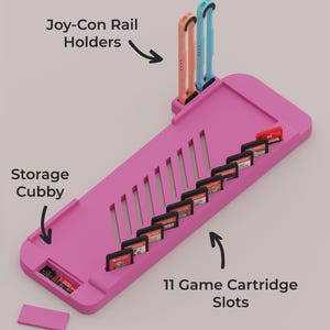 May include: A pink gaming console accessory base featuring the text Pro Base Features, Joy-Con Rail Holders, Storage Cubby, and 11 Game Cartridge Slots. It includes two vertical rail holders, a storage area, and eleven slots for game cartridges.