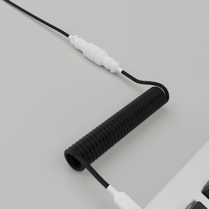 May include: A black coiled cable with white connectors, connected to a white keyboard. The cable has a coiled section and a straight section. The keyboard has black keys and a white frame. The image is set against a gray background.