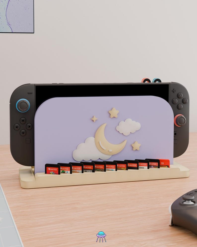 May include: A light purple gaming console stand featuring a crescent moon, clouds, and stars design. The stand holds a black gaming console and includes a row of ten small rectangular game cartridges in a light-colored wooden base.