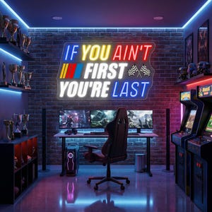May include: A gaming room with a neon sign that reads "IF YOU AIN'T FIRST YOU'RE LAST". The room features a computer setup with multiple monitors, a gaming chair, and arcade machines. Trophies are displayed on shelves, and the walls are brick.
