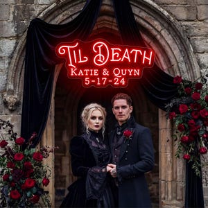 May include: A couple stands beneath a neon sign that reads "Til Death" with the names "Katie & Quyn" and the date "5-17-24". They are dressed in black formal attire, surrounded by red roses and dark draping.
