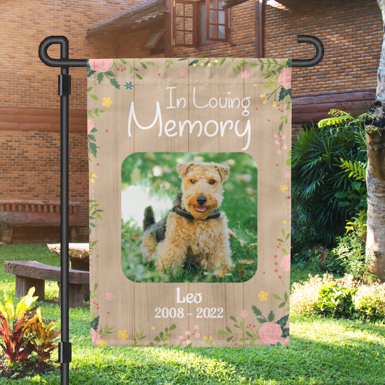 Puede incluir: Una bandera de jard&iacute;n conmemorativa con fondo de madera y detalles florales. Una foto de un perro marr&oacute;n y blanco est&aacute; en el centro con el texto "In Loving Memory" arriba y "Leo 2008-2022" abajo.