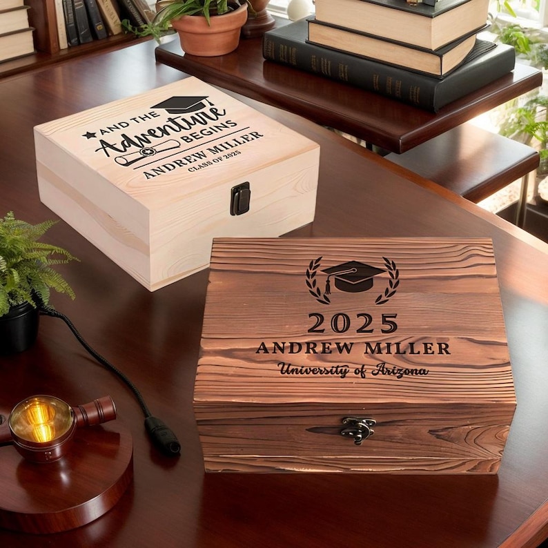 May include: Two wooden boxes with engraved graduation messages. The top box is light wood with the text "And the Adventure Begins, Andrew Miller, Class of 2025". The bottom box is dark wood with the text "2025, Andrew Miller, University of Arizona".