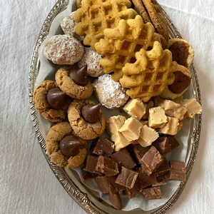 May include: A silver platter filled with a variety of cookies and fudge. The cookies include chocolate chip, peanut butter, and sugar cookies. The fudge is in squares and is both milk chocolate and white chocolate.