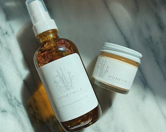 May include: Two skincare products, a clear glass bottle with a white pump top and a white jar with a gold lid. The bottle is labeled "Honeywild Wild Oil Cleanser for oily and combination skin". The jar is labeled "Honeywild Rosewater Moist".