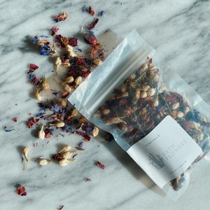 May include: A clear plastic bag filled with dried flower petals, including red, white, and blue petals. The bag is labeled "Honey Wild Bath Flowers Natural Relaxing".
