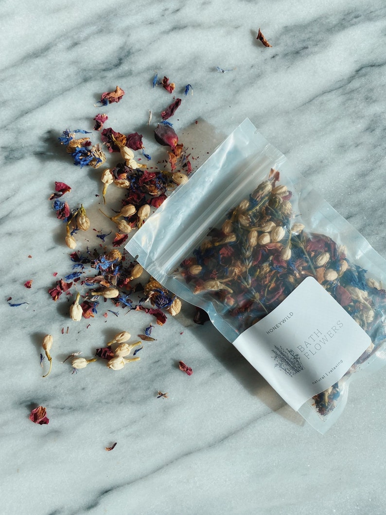 May include: A clear plastic bag filled with dried flower petals, including red, white, and blue petals. The bag is labeled "Honey Wild Bath Flowers Natural Relaxing".