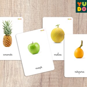 May include: Five flashcards with images of different fruits and their names in Portuguese. The fruits are pineapple, melon, apple, and loquat. The cards are white with a red and yellow logo in the top right corner.