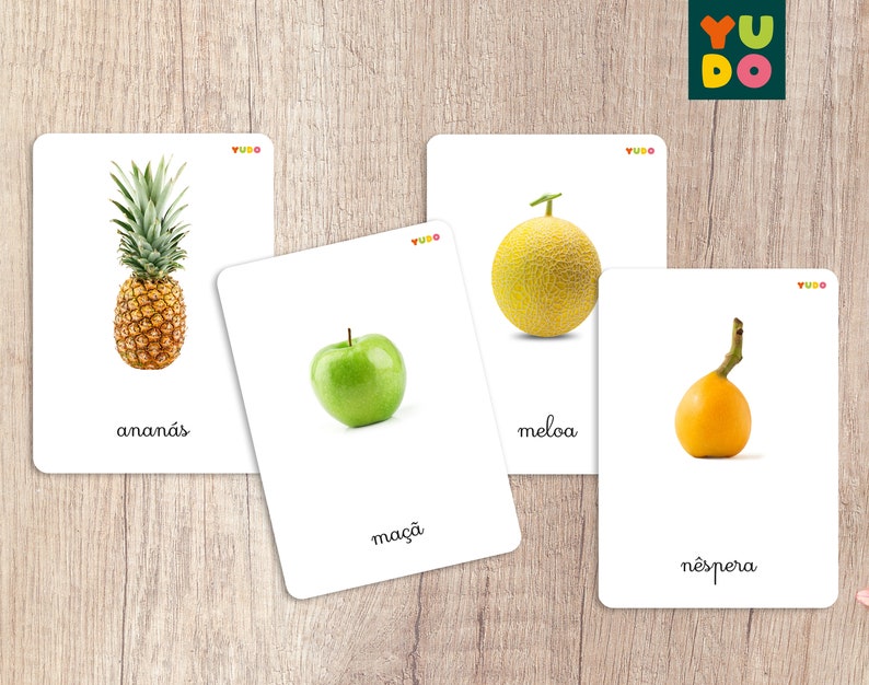 May include: Five flashcards with images of different fruits and their names in Portuguese. The fruits are pineapple, melon, apple, and loquat. The cards are white with a red and yellow logo in the top right corner.