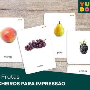 May include: A set of printable flashcards featuring different fruits in Portuguese. The cards show a mango, grapes, a pear, and a blackberry. Each card has the name of the fruit written below the image.
