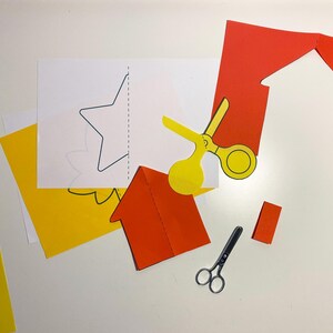 Pode incluir: Uma coleção de recortes de papel coloridos e materiais de artesanato, incluindo papel amarelo e vermelho, tesouras e um modelo de estrela e casa. A imagem sugere um projeto de artesanato DIY ou uma atividade educacional.