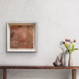 Op de afbeelding: Een ingelijst abstract schilderij met een bruin en beige kleurenschema hangt aan een witte muur boven een houten consoletafel. Twee keramische vazen en een boeket paarse en gele tulpen staan op de tafel.