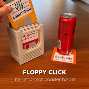 May include: A beige plastic storage container shaped like a computer drive, holding several colorful floppy disk coasters. One orange coaster labeled Beer.rar sits on the surface with a 330 ml red soda can placed on top of it for scale.