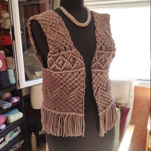 May include: A light brown crocheted vest with fringe detailing. The vest is sleeveless and has a V-neck.