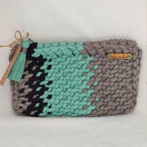 Puede incluir: Una bolsa de crochet gris, verde y negra con una etiqueta de cuero marrón que dice "miss me much".