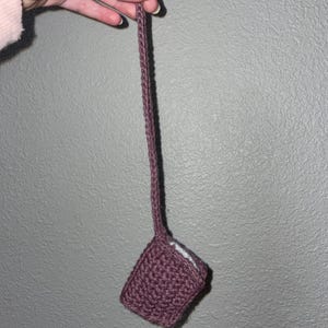 May include: A small, crocheted pouch with a long strap, made in a dusty rose color.