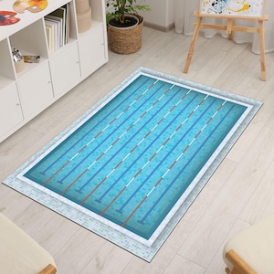 Puede incluir: Una alfombra rectangular con un diseño de piscina. La alfombra presenta un patrón de agua azul con líneas de carril blancas y rojas. El borde es un patrón de mosaico, creando una apariencia de piscina realista. La alfombra está colocada sobre un suelo de madera clara.