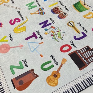 May include: A light gray educational rug featuring musical instruments and the alphabet. Instruments include a xylophone, saxophone, ukulele, and organ. The rug has a piano keyboard border and colorful letters.