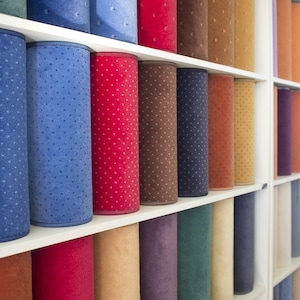 Puede incluir: Una pared de estantes llena de rollos de alfombra en varios colores, incluyendo azul, rojo, marr&oacute;n, beige y morado.