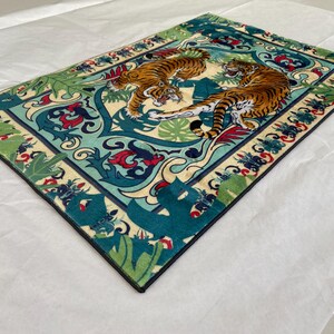 May include: Rectangular rug featuring two orange tigers with black stripes set against a teal and cream background. The rug has a detailed border with floral and leaf patterns in red, green, and blue. The design evokes a sense of nature and wildlife.