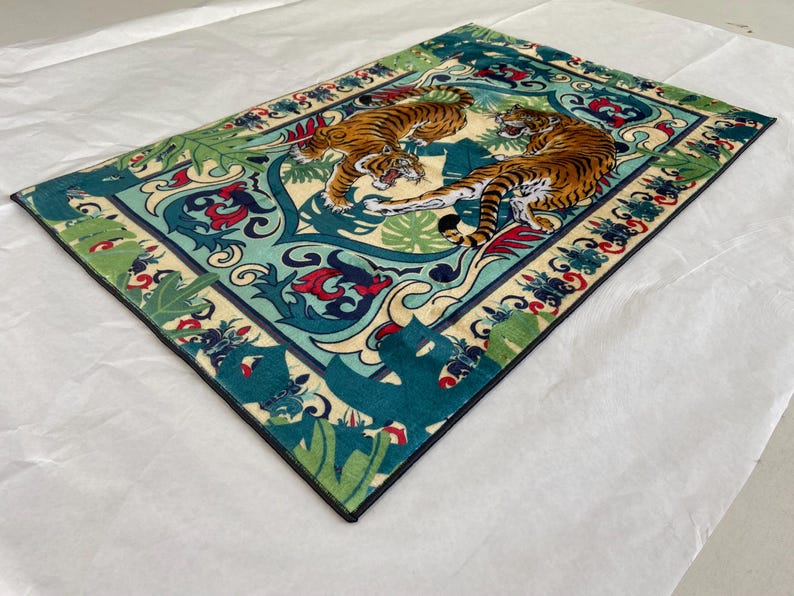 May include: Rectangular rug featuring two orange tigers with black stripes set against a teal and cream background. The rug has a detailed border with floral and leaf patterns in red, green, and blue. The design evokes a sense of nature and wildlife.